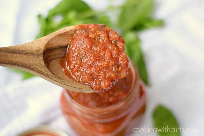 Homemade Pizza Sauce on a wooden spoon over a jar of sauce.