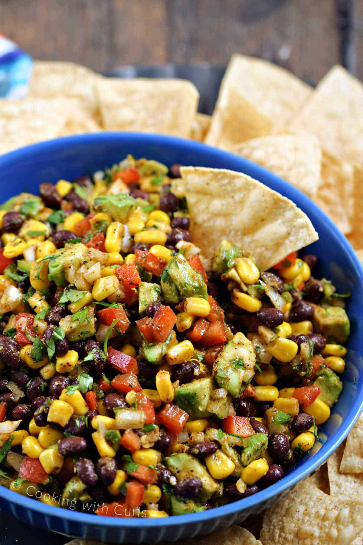 A serving bowl filled with black bean and corn salsa surrounded by tortilla chips.