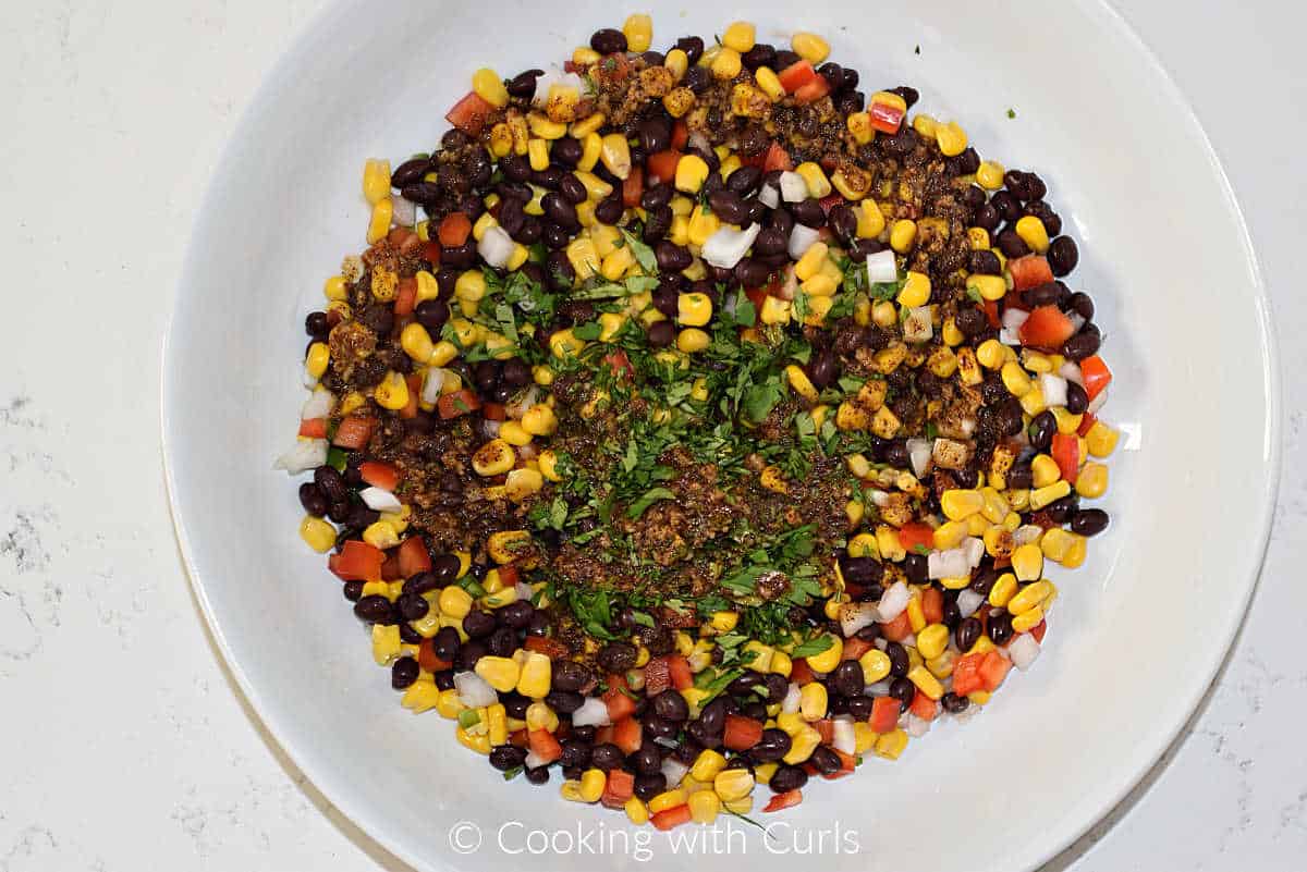Black bean and corn salsa topped with cilantro and dressing in a mixing bowl.