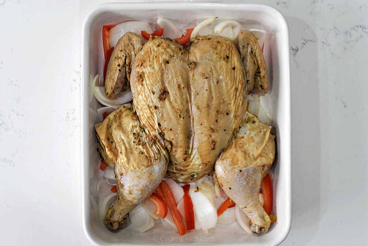 Marinated chicken in a baking dish with onion and pepper slices.