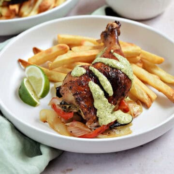 Roast chicken leg with green sauce on a bed of fries.