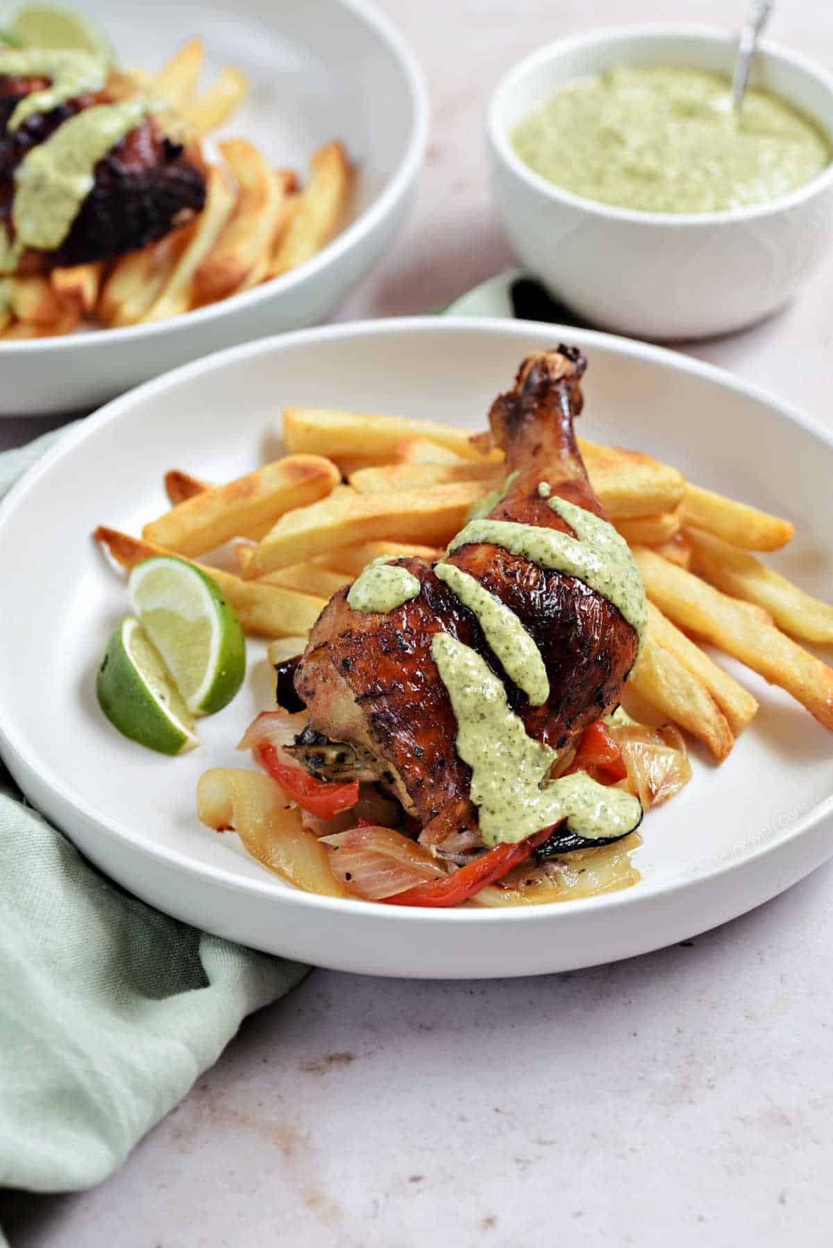 Roast chicken leg with green sauce on a bed of fries.