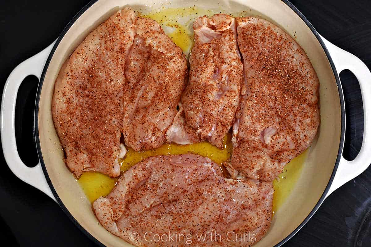 Chicken breasts coated with seasoning in a cast iron skillet with olive oil.