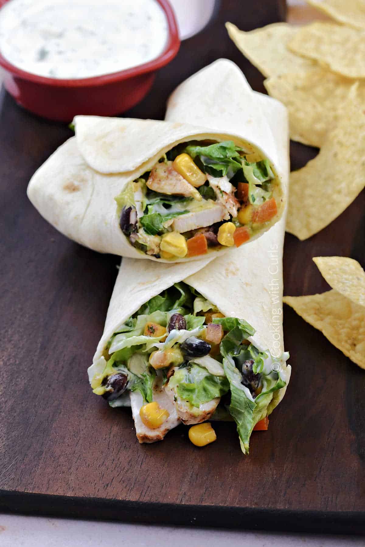 Chicken, corn, black beans, lettuce, and ranch dressing wrapped in a flour tortilla and cut in half on a wood board.
