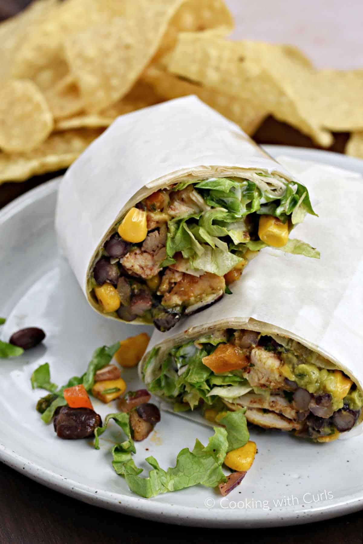 A southwest chicken wrap cut in half and stacked on top of each other on a plate with tortilla chips in the background.