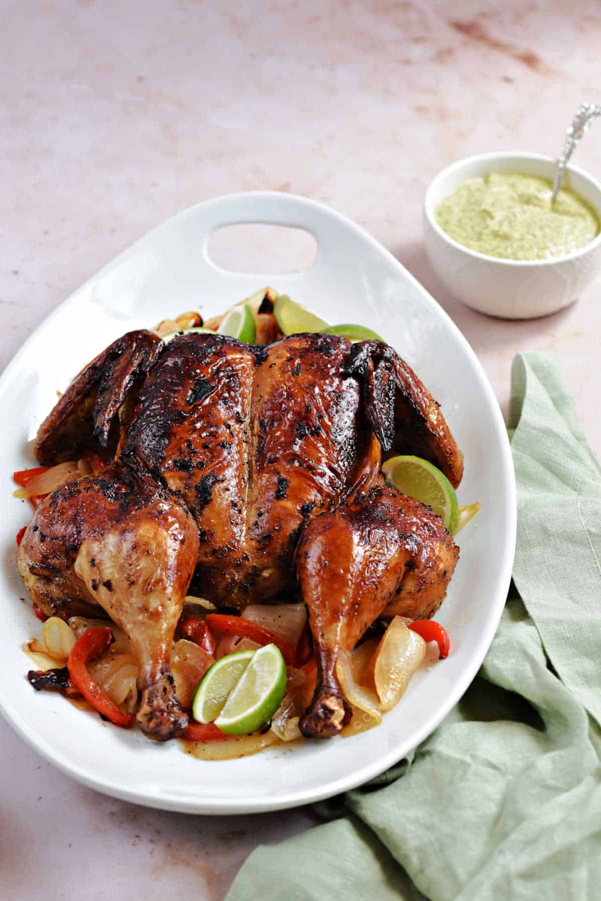 Butterflied roast chicken on a serving platter with green sauce on the side.