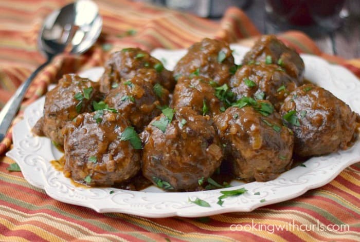 meatballs on a white platter sitting on a striped napkin with a serving spoon on the side.