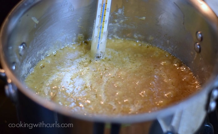 Caramel simmering in a saucepan with a candy thermometer on the side.