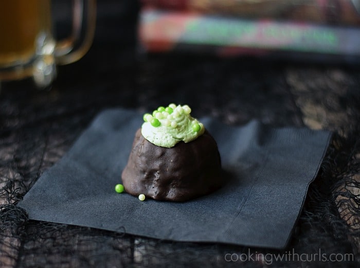 A chocolate covered cupcake topped with green frosting and decorative ball candies sitting on a black napkin.