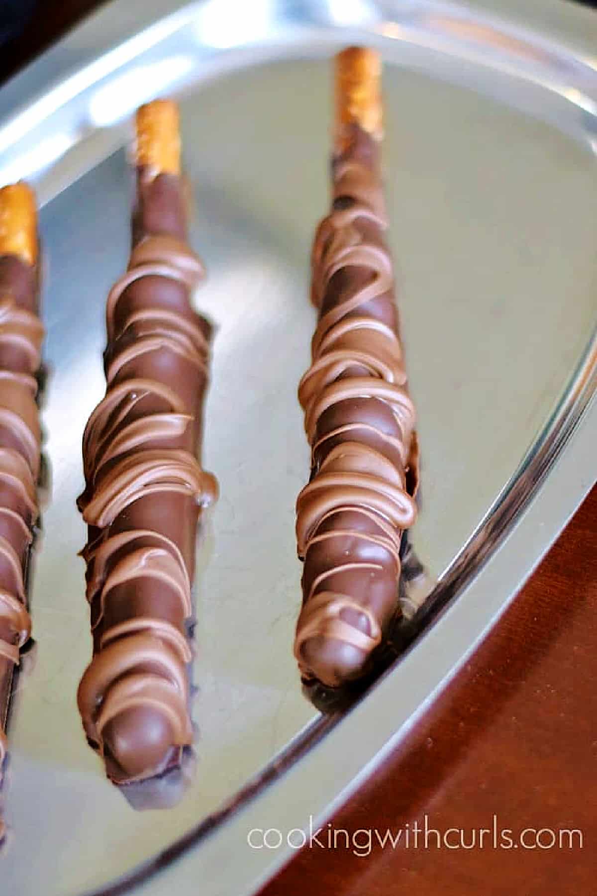 Three Chocolate Caramel Pretzel Rods on a silver tray. 