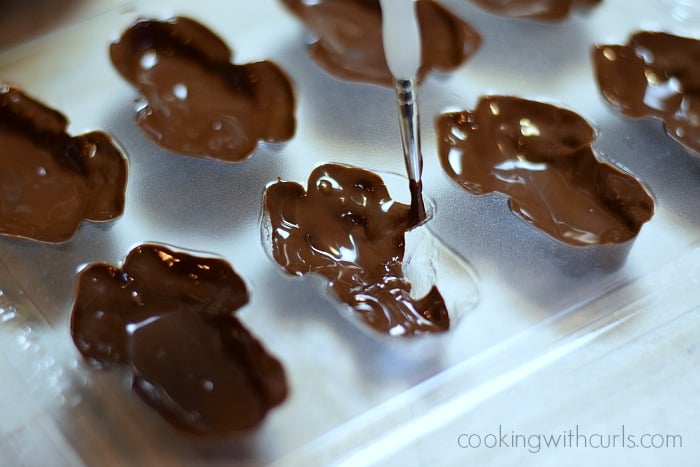 A paintbrush spreading the melted chocolate around in the frog molds.