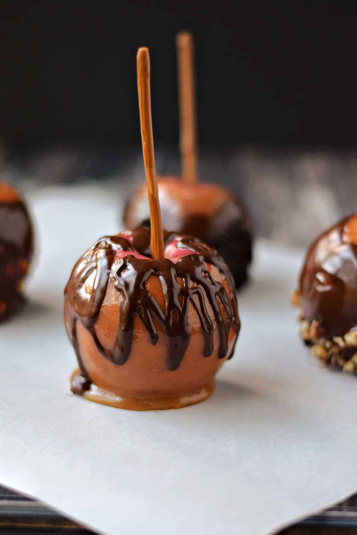 Four chocolate covered caramel apples with nuts and sprinkles.