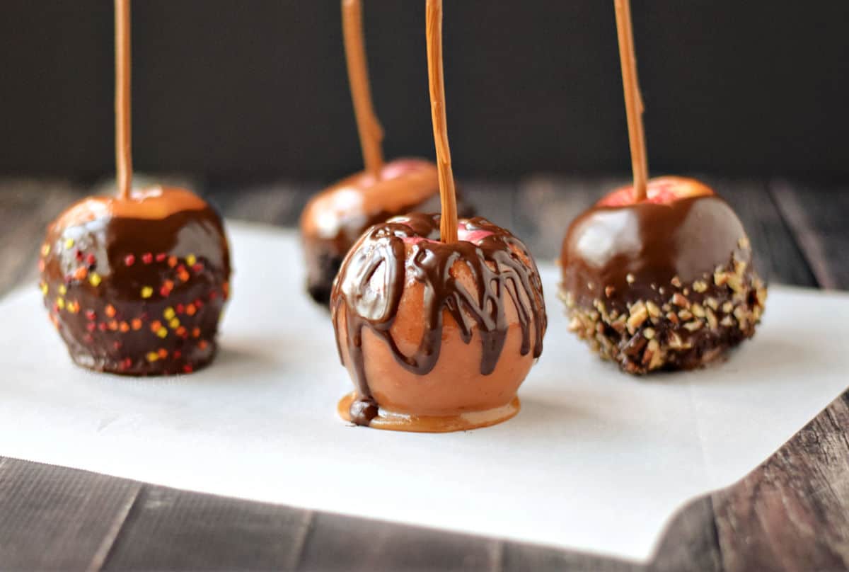 Four gourmet caramel apples on parchment paper.