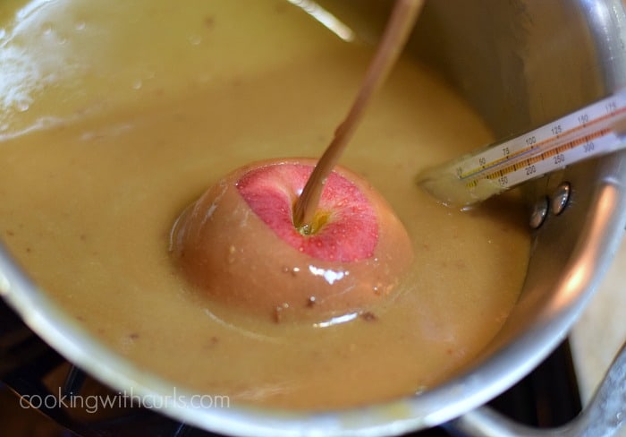 An apple with a stick in the center being dipped into the hot caramel