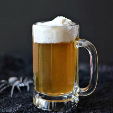 A glass beer mug filled with a caramel colored cocktail topped with whipped cream.