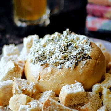 Spinach dip in a bread bowl surrounded by torn bread pieces.