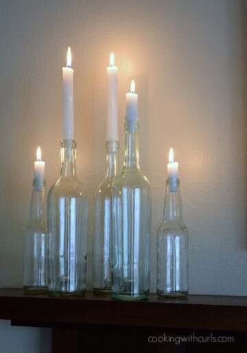 Lit Candles in glass bottles on a fireplace mantle.