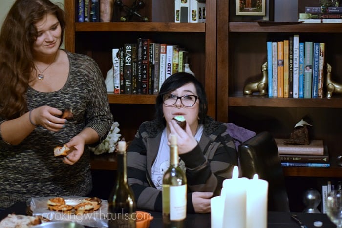 Two girls sitting at a table with lots of candles, eating pizza rolls and cauldron cakes.