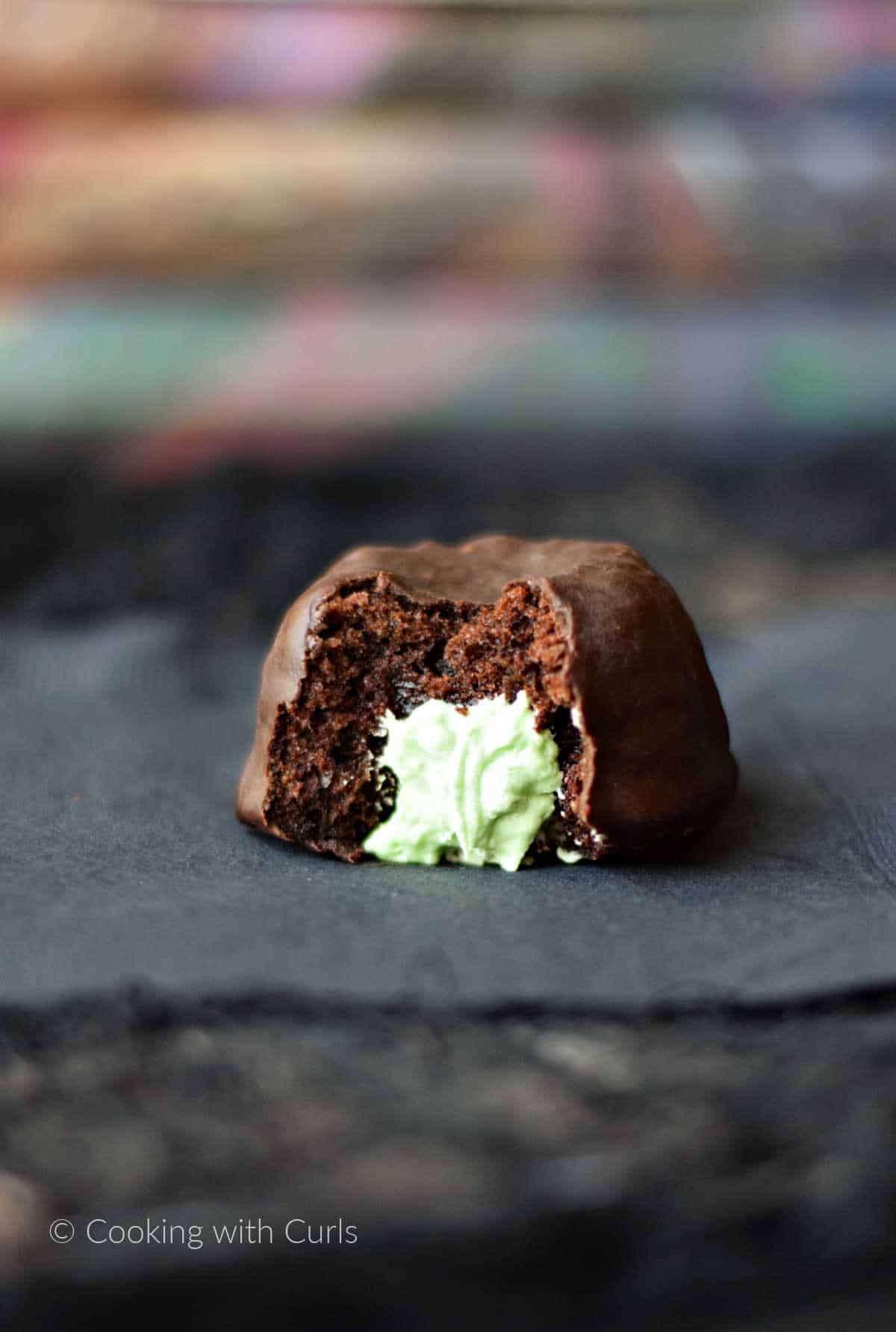 A chocolate covered cupcake with green frosting oozing out of the center on a black napkin with Harry Potter books in the background.