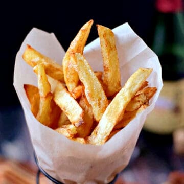 Homemade French Fries wrapped in parchment paper inside a wire cone holder.