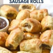 A pile of puff pastry sausage rolls in a parchment lined basket with dipping sauce on the side and title graphic across the top.