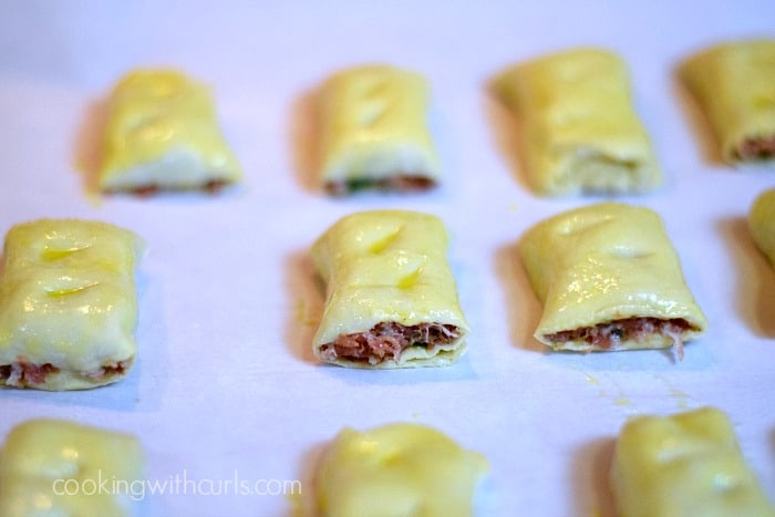 Eleven egg washed topped Puff Pastry Sausage Rolls on a parchment paper lined baking sheet.