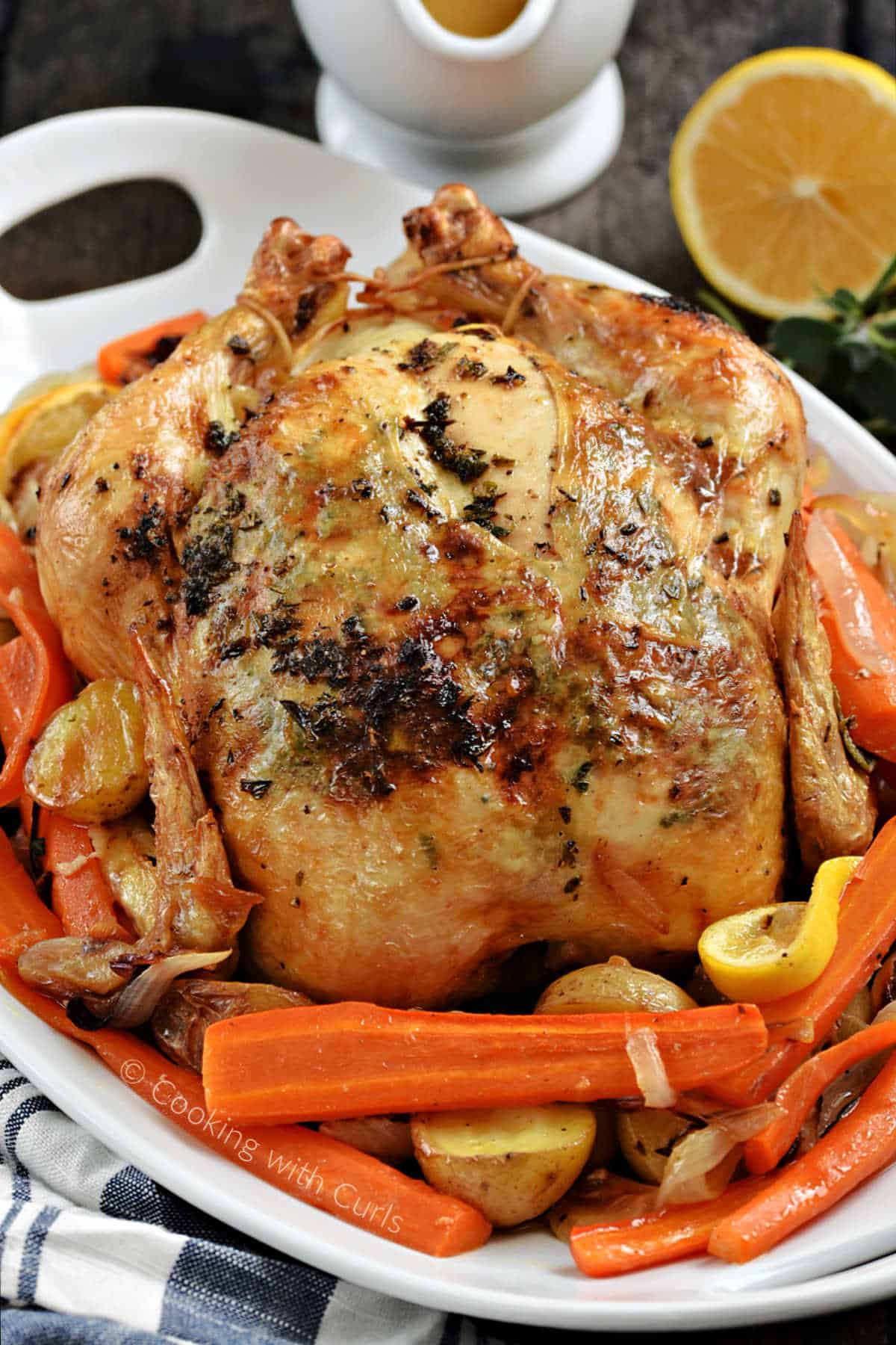 Roast chicken on a bed of carrots and potatoes with gravy and a lemon in the background.
