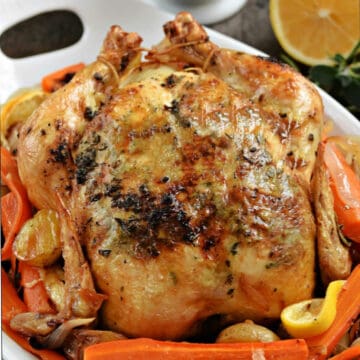 Roast chicken on a bed of carrots and potatoes with a lemon in the background.