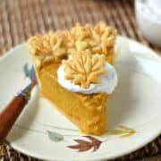 A slice of Dairy-free Pumpkin Pie topped with coconut cream and a leaf shaped cookie.