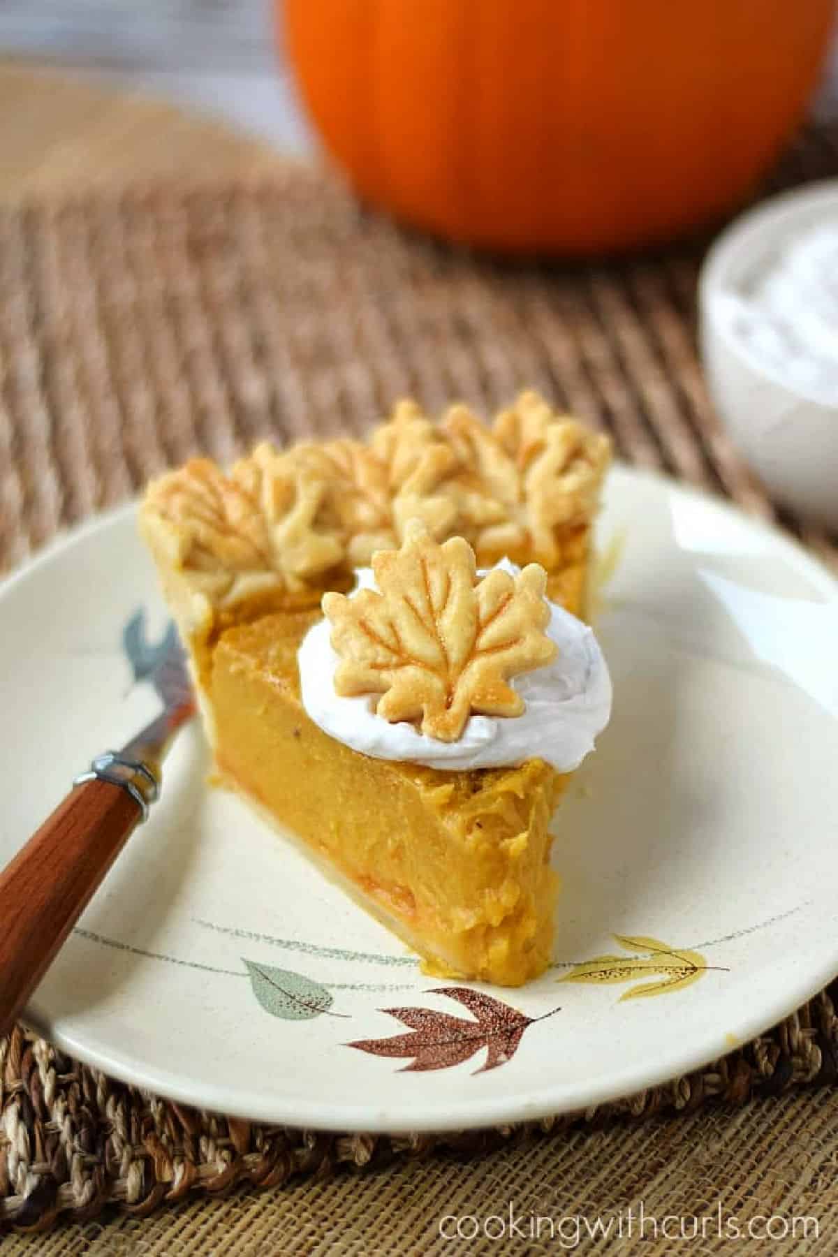 A slice of Dairy-free Pumpkin Pie topped with coconut cream and a leaf shaped cookie. 