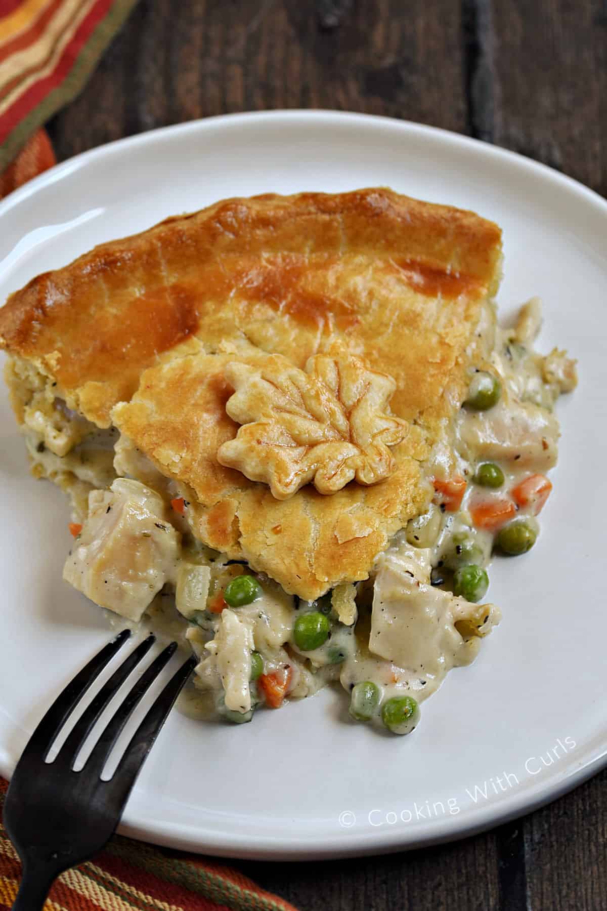A slice of turkey pot pie on a small plate with a maple leaf cut-out on top. 