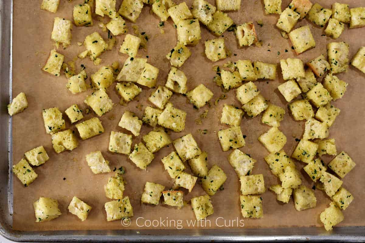 Bread-cubes-tossed-in-butter-oil-and-herbs-on-a-parchment-lined-baking-sheet.
