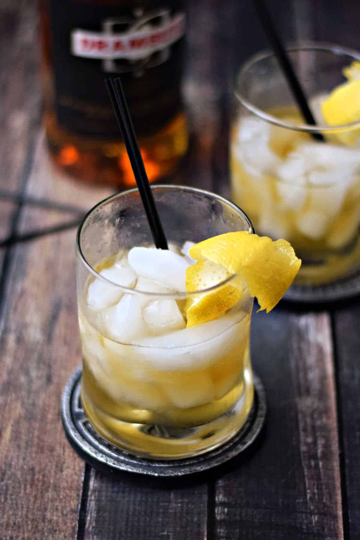 Two glasses with golden cocktail, ice cubes and lemon twist.