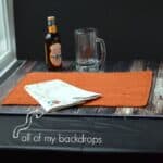 backdrop on table with an orange place mat, bottle of beer, empty glass mug and a black board as a back drop