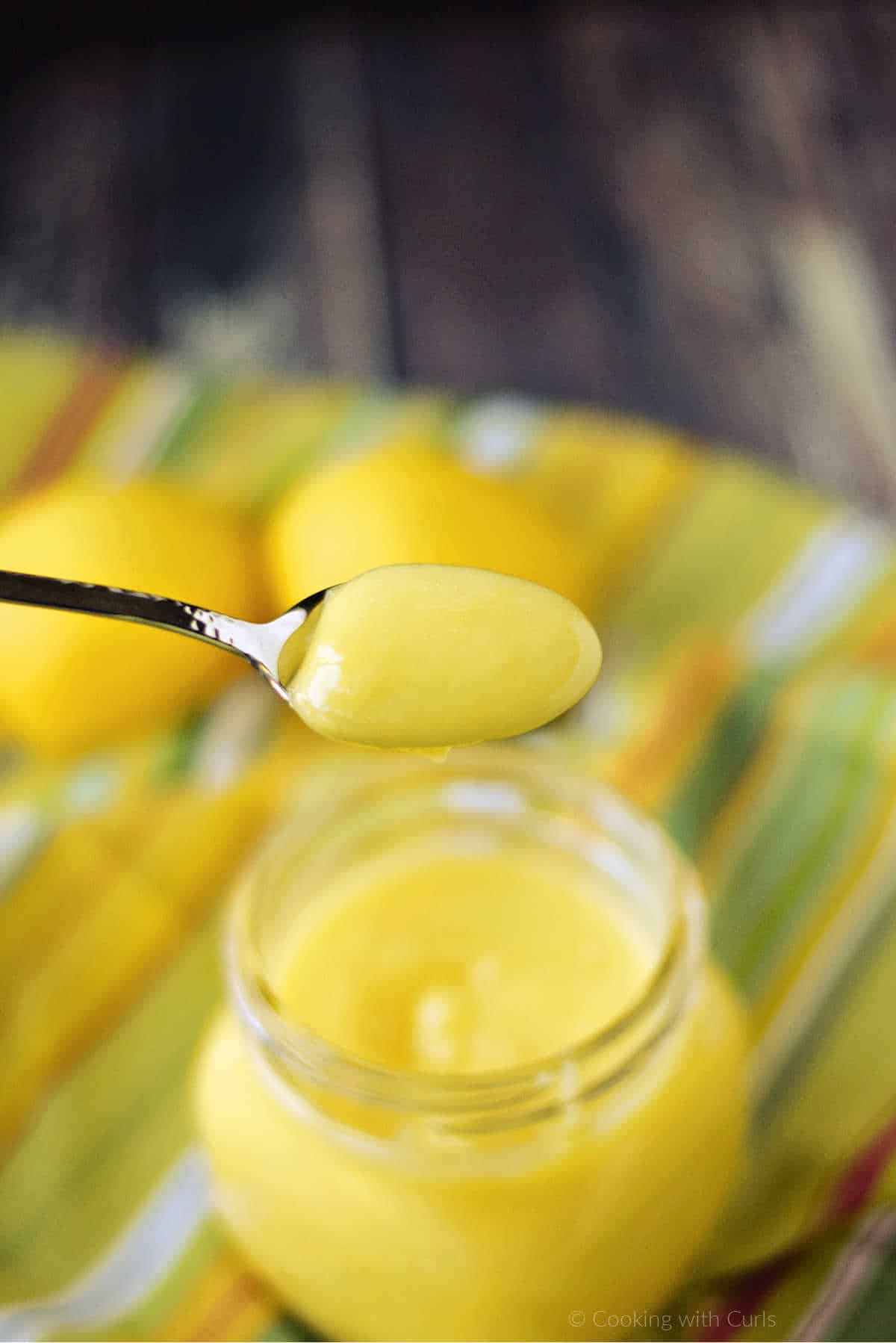 A scoop of homemade lemon curd on a spoon over the filled jar.