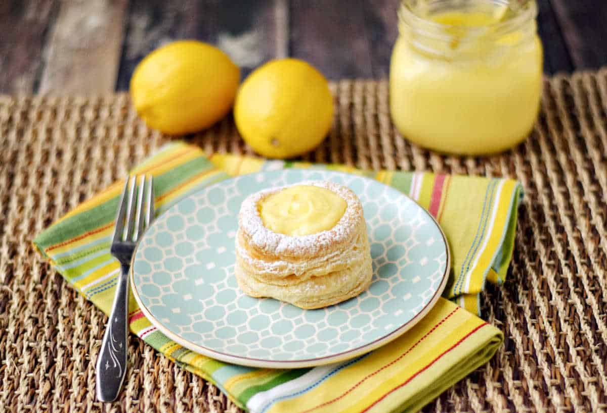 Lemon curd puff pastry tart on a small dessert plate with jar of lemon curd in the background.