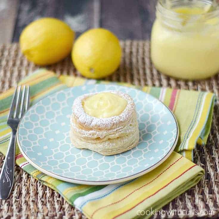 A lemon curd filled puff pastry tart on a plate with a jar of lemon curd in the background.