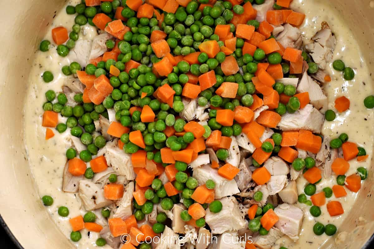 Peas, carrots, and turkey chunks in a creamy sauce inside a Dutch oven. 