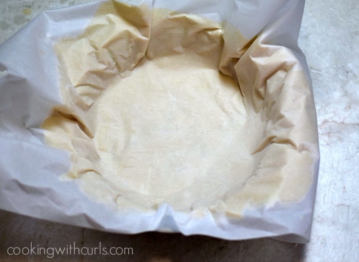 Pie crust rolled out in between two sheets of parchment paper sitting in a pie dish. 