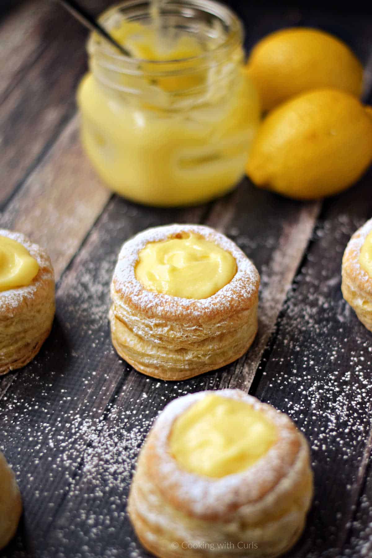 Puff pastry tarts filled with lemon curd and sprinkled with powdered sugar and jar of lemon curd in the background.