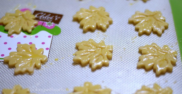 Maple leaf pie crust cutouts on a baking sheet brushed with egg wash.