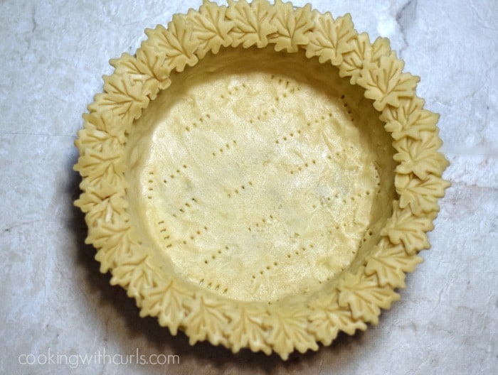 Looking down on a pie dish with pie crust dough poked with holes in the center and maple leaf cut outs around the rim.