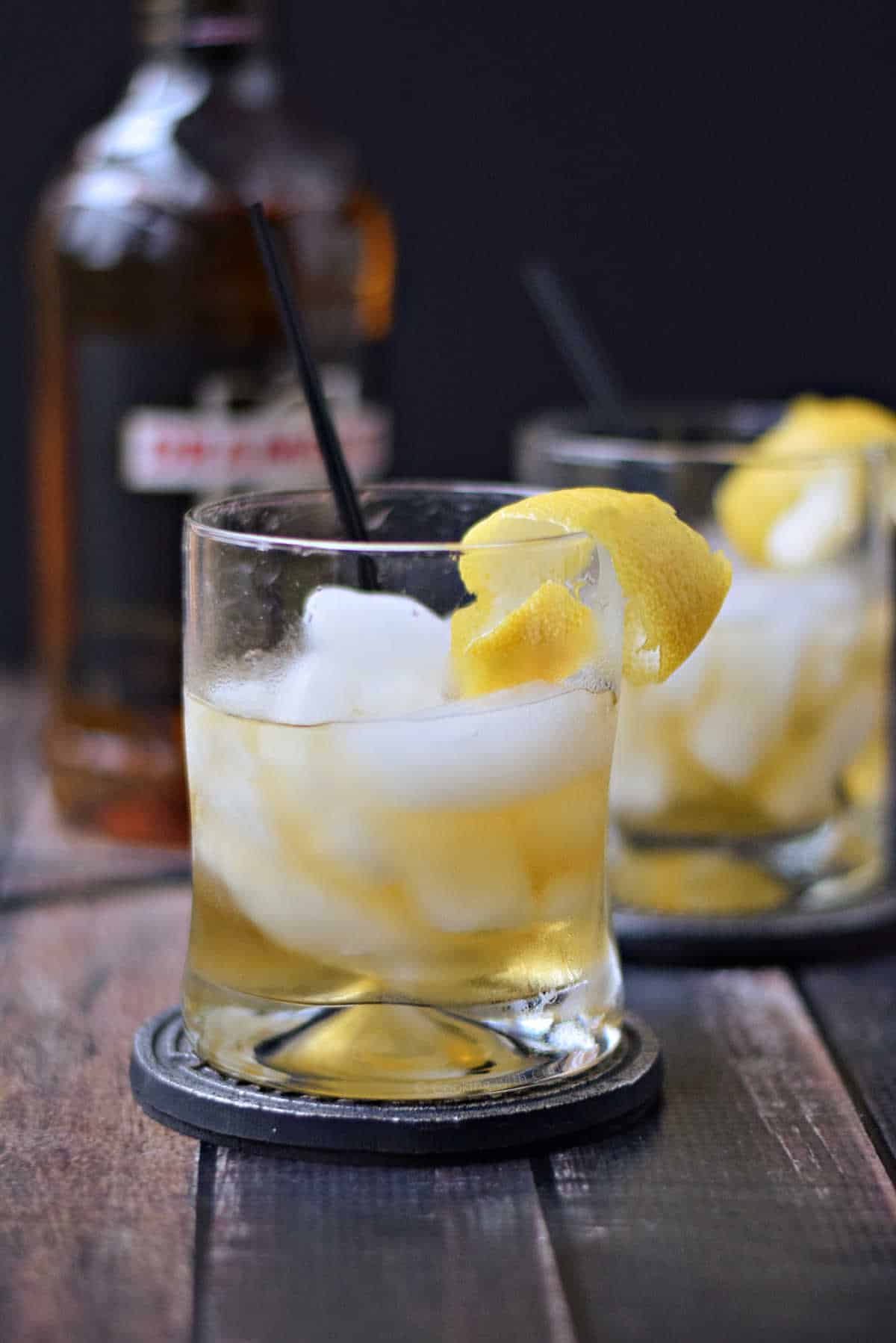 Two golden cocktails in front of a bottle of Drambuie.