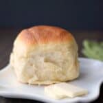 a dinner roll sitting on a small, white plate with two pats of butter