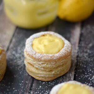 Lemon curd puff pastry tarts on a wood board with an empty jar and lemon in the background.
