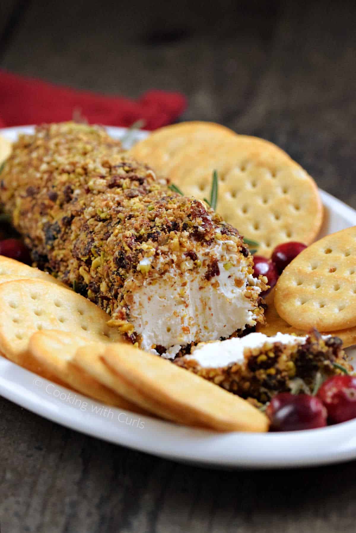 A cut cranberry pecan goat cheese log on an oval plate with crackers.
