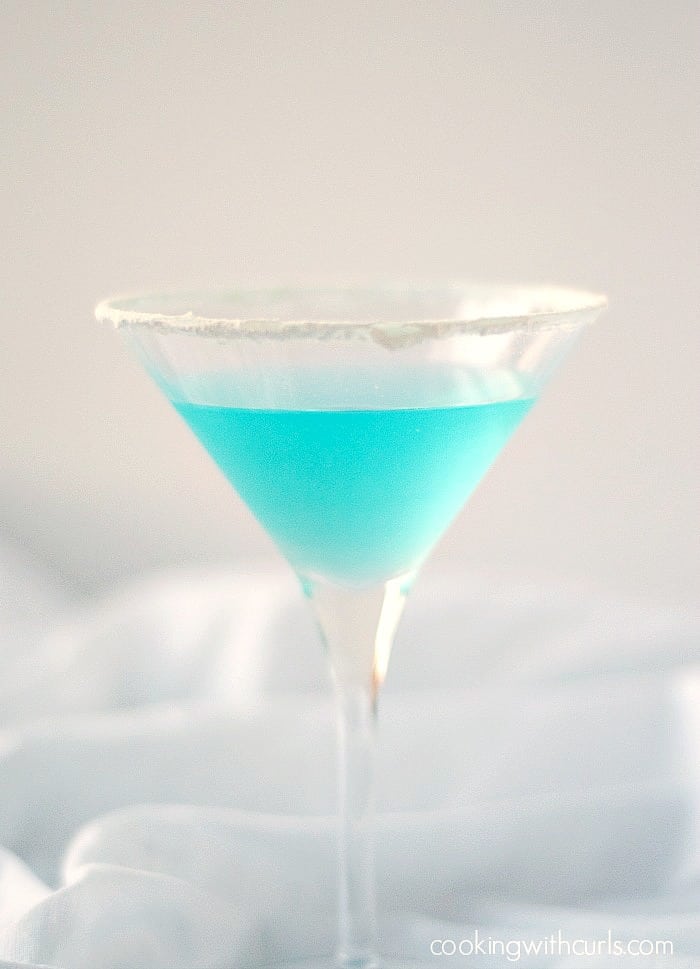 Clear blue cocktail strained into a sugar-rimmed martini glass.