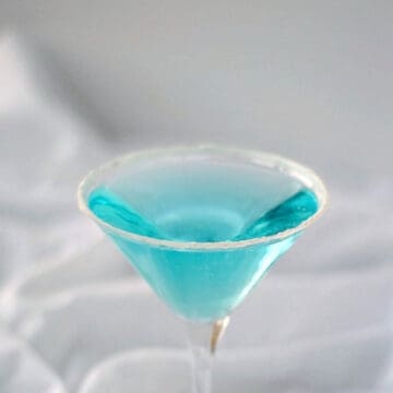clear blue cocktail in a martini glass with a sugar coated rim.