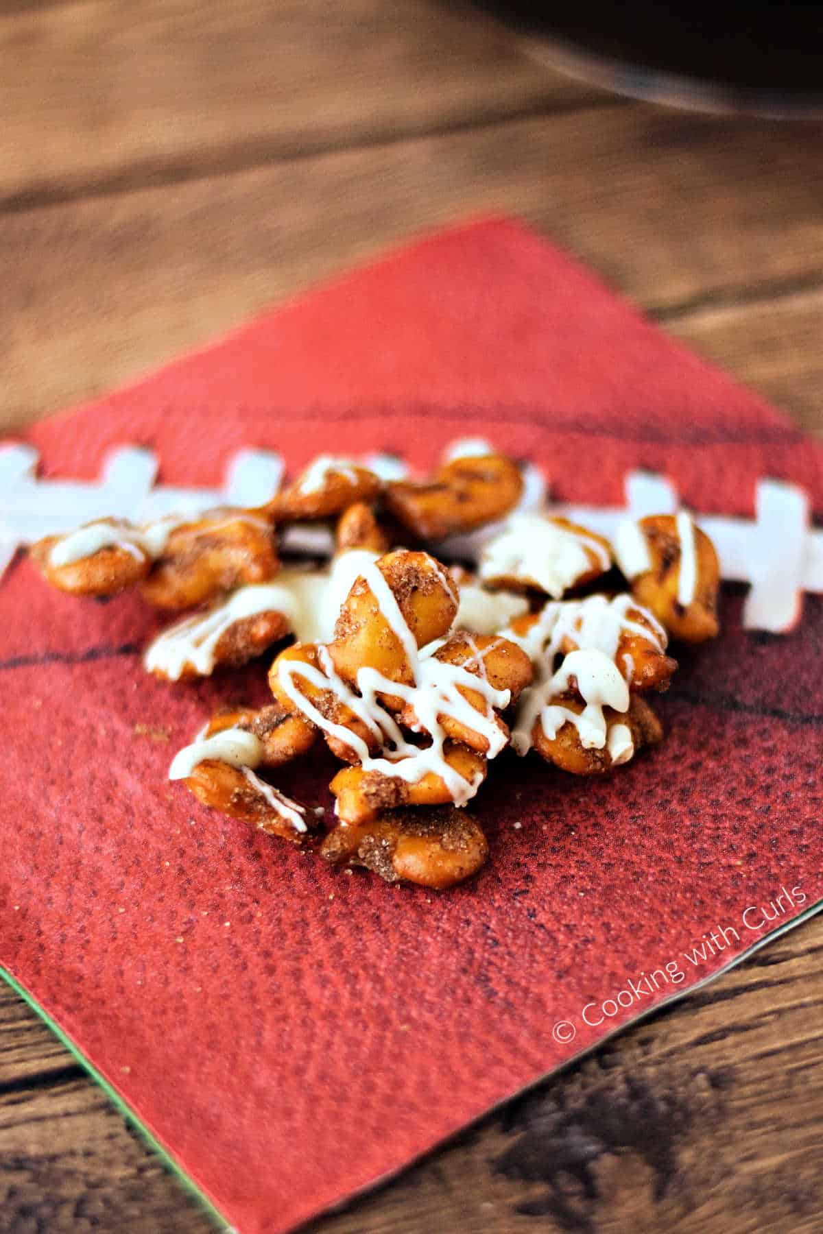 A handful of cinnamon sugar topped goldfish pretzel crackers topped with white chocolate on a football napkin. 