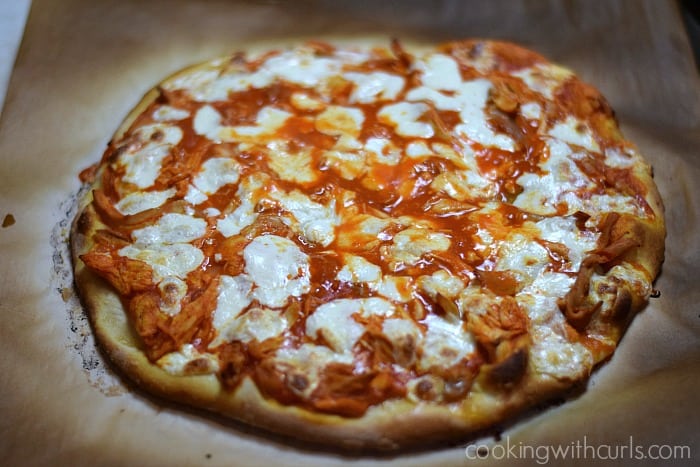 Buffalo Chicken Pizza with melted cheese on a sheet of charred parchment paper.